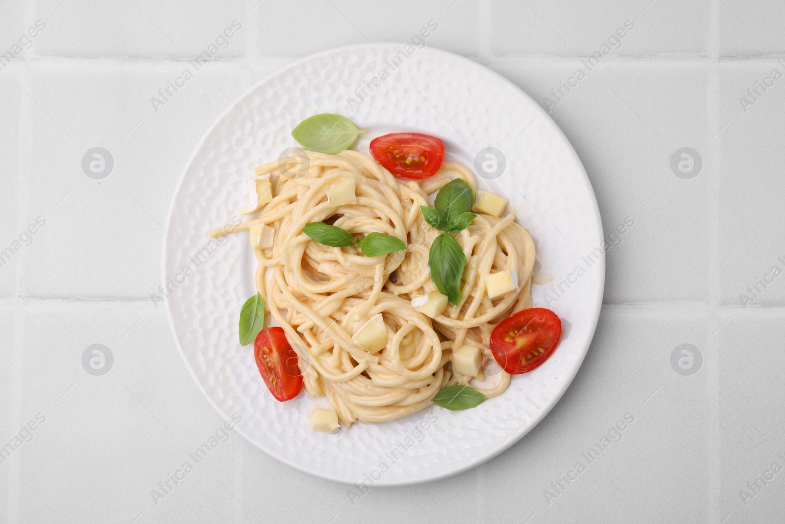 Photo of Delicious pasta with brie cheese, tomatoes and basil leaves on white tiled table, top view