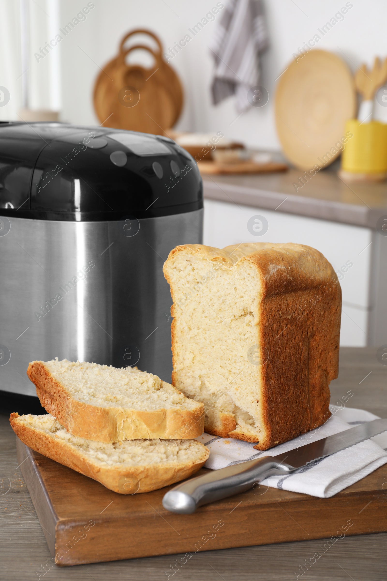 Photo of Breadmaker and cut homemade bread on wooden table in kitchen