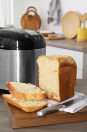 Photo of Breadmaker and cut homemade bread on wooden table in kitchen