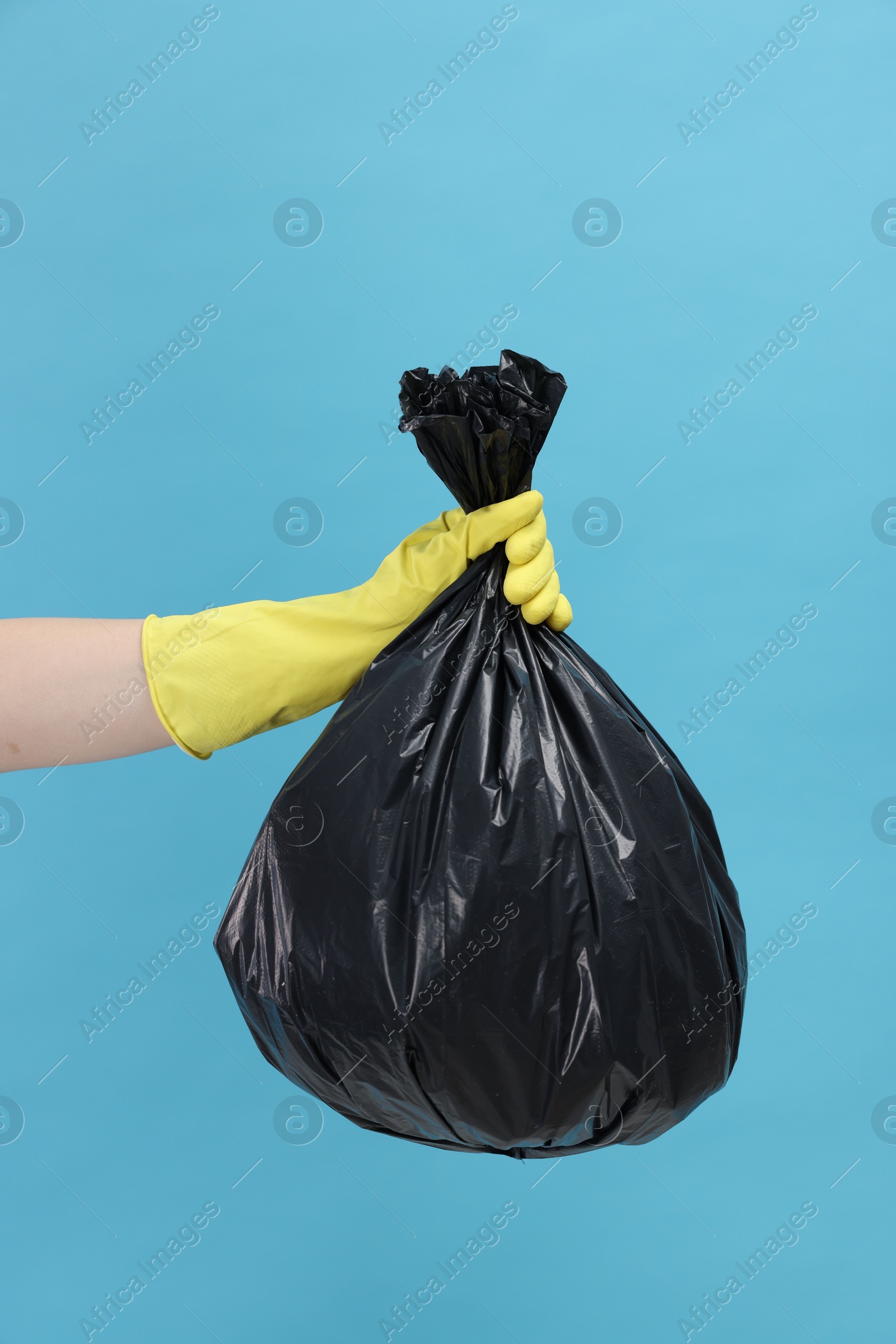 Photo of Woman holding plastic bag full of garbage on light blue background, closeup