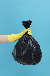 Photo of Woman holding plastic bag full of garbage on light blue background, closeup