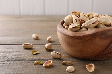 Photo of Tasty pistachios in bowl on wooden table, closeup. Space for text