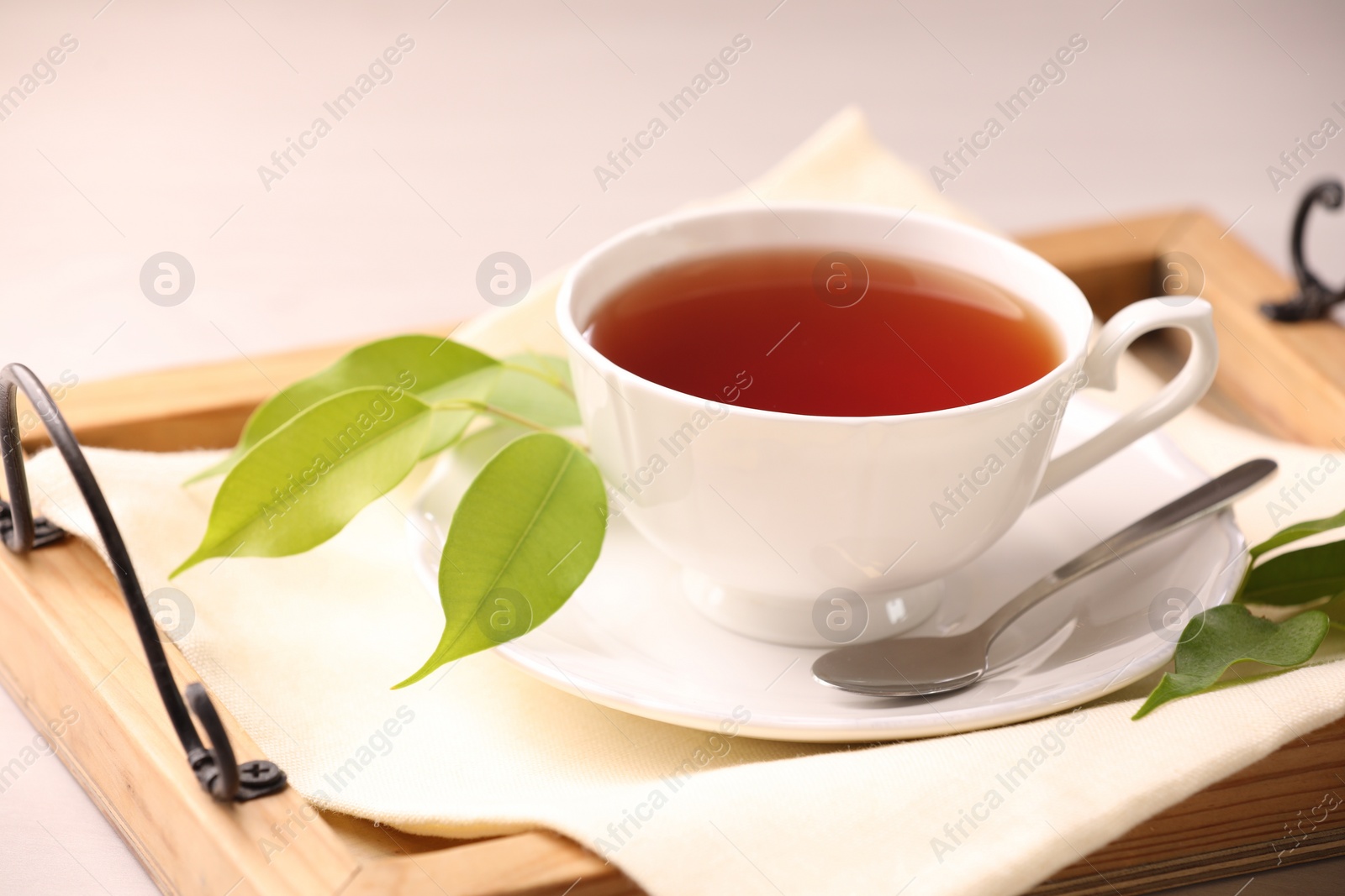 Photo of Aromatic tea in cup, saucer, spoon and green leaves on table