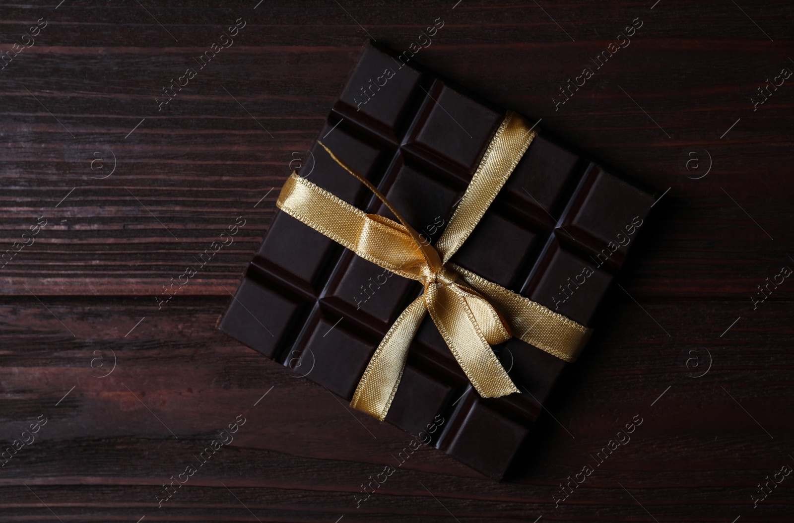 Photo of Tasty dark chocolate bar with ribbon on wooden table, top view