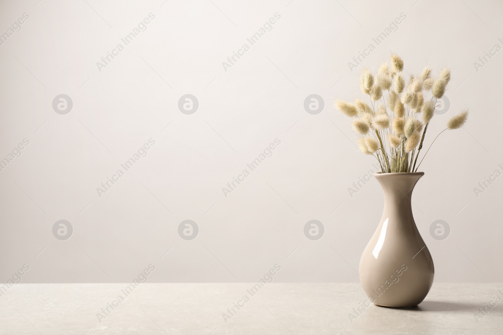 Photo of Dried flowers in vase on table against light background. Space for text