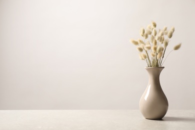 Dried flowers in vase on table against light background. Space for text