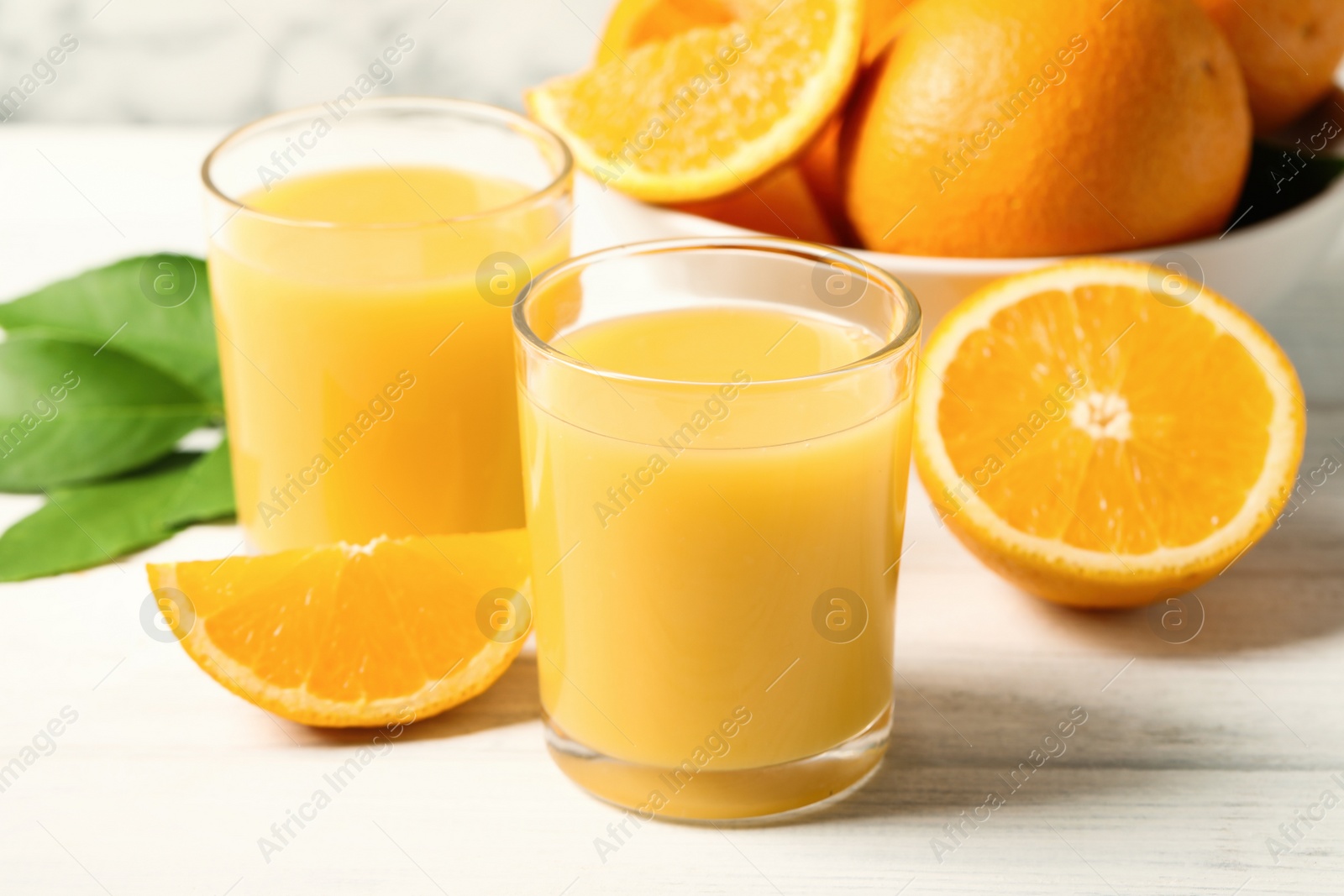 Photo of Glasses of orange juice and fresh fruits on white wooden table, closeup