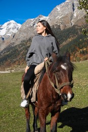 Photo of Young woman riding horse in mountains on sunny day. Beautiful pet