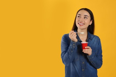 Happy woman with tasty yogurt on orange background. Space for text