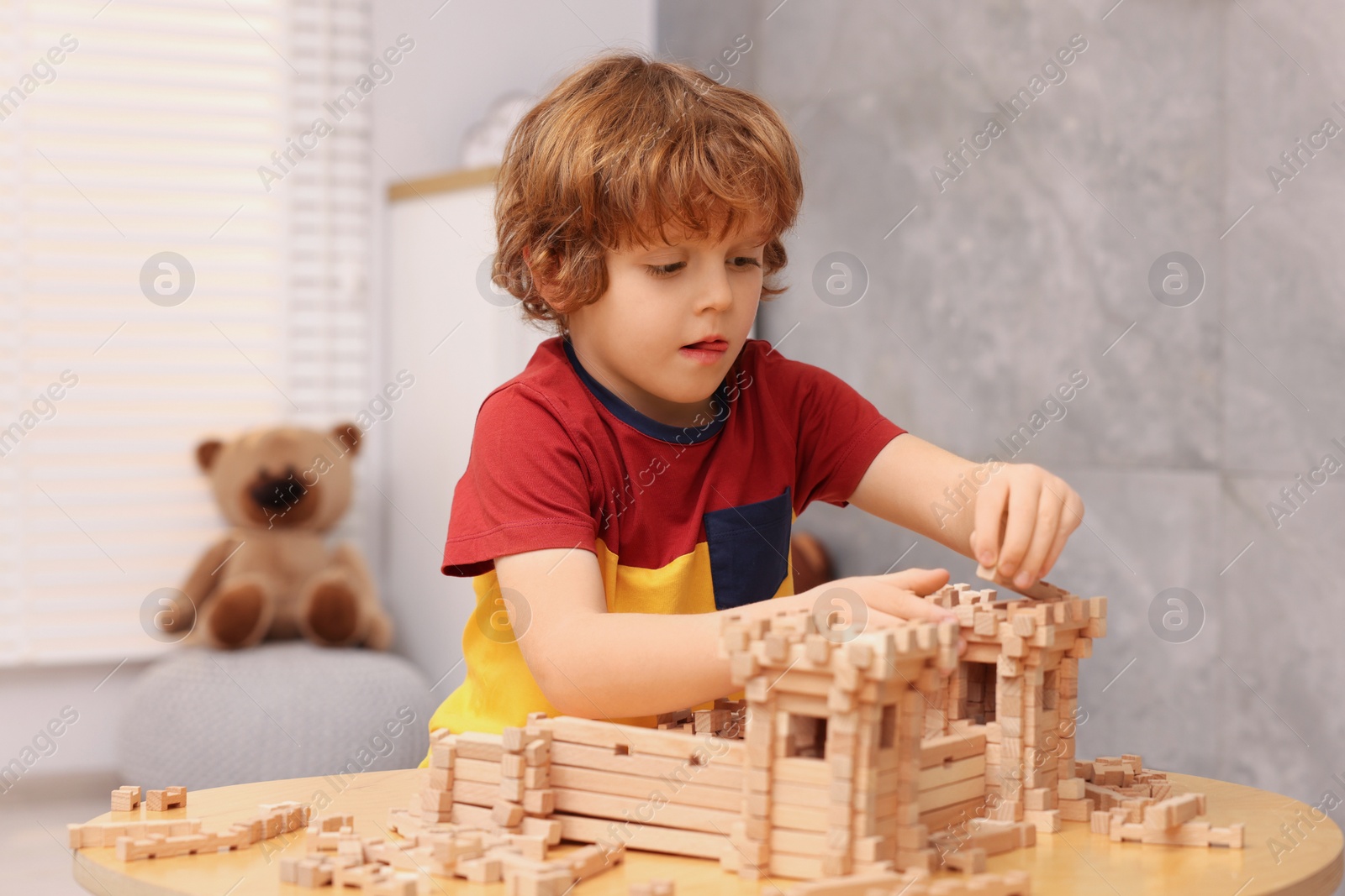 Photo of Cute little boy playing with wooden construction set at table in room. Child's toy