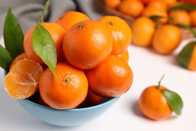 Photo of Fresh ripe juicy tangerines and green leaves in bowl on white table, closeup. Space for text