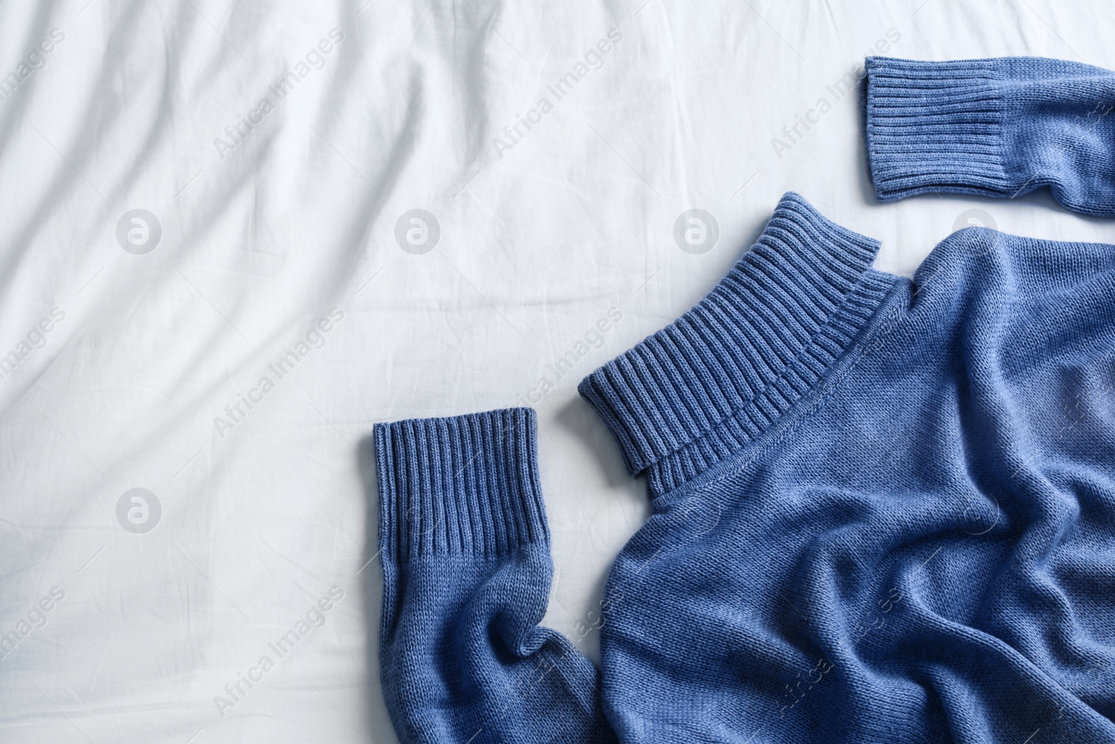 Photo of Blue warm sweater on white crumpled fabric, top view. Space for text