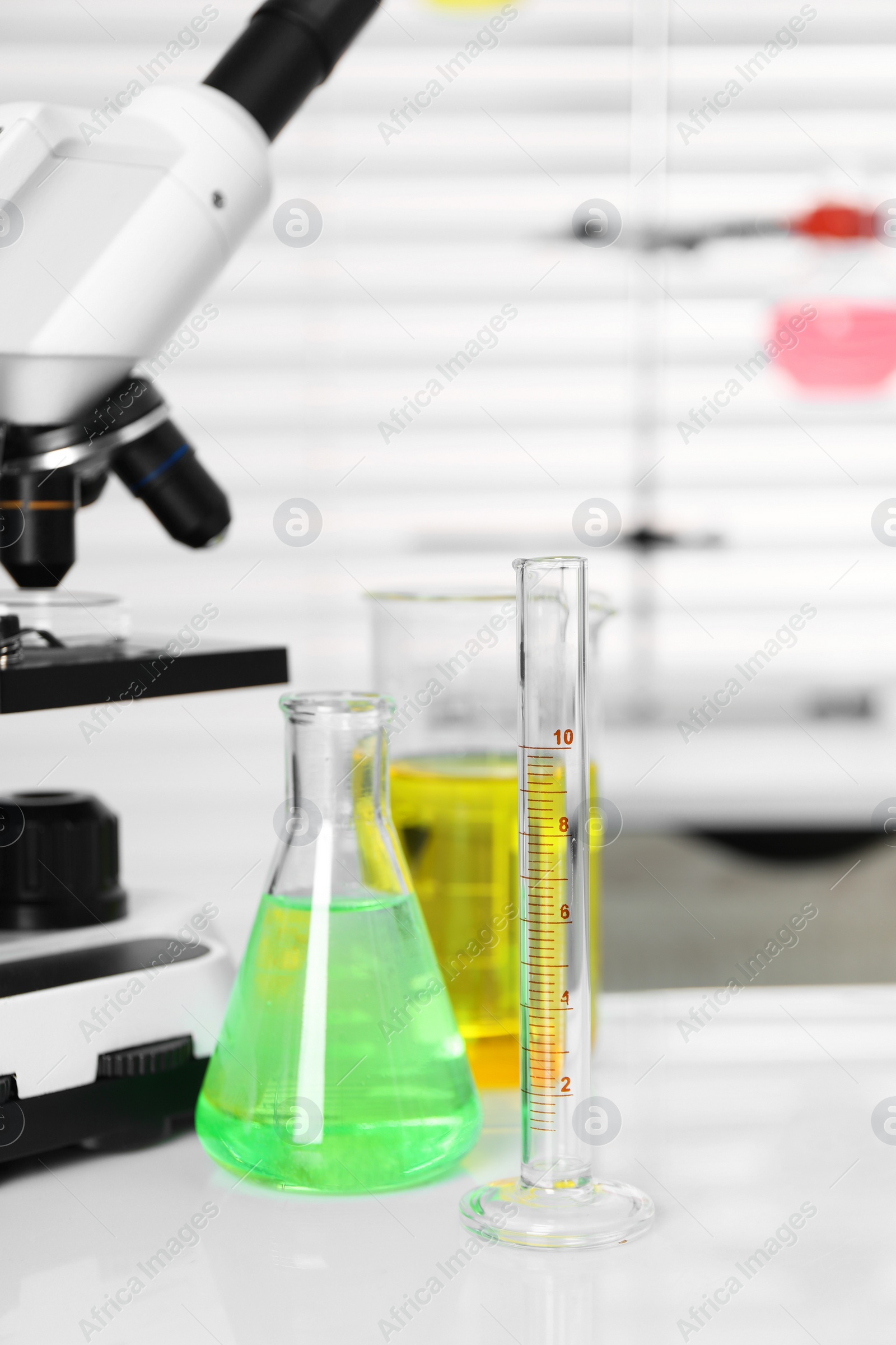 Photo of Laboratory analysis. Different glassware with liquids and microscope on white table indoors