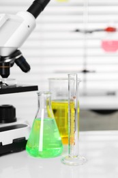 Photo of Laboratory analysis. Different glassware with liquids and microscope on white table indoors