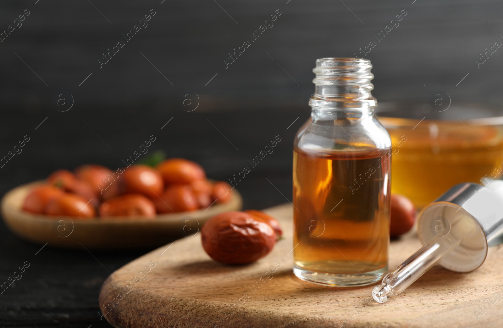 Photo of Glass bottle with jojoba oil and seeds on black wooden table. Space for text