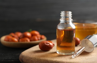 Photo of Glass bottle with jojoba oil and seeds on black wooden table. Space for text