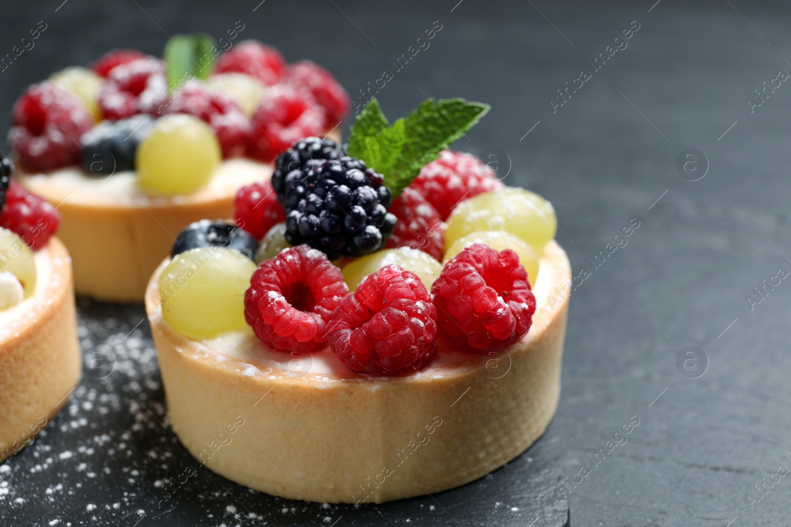 Photo of Delicious tartlets with berries on black table, closeup