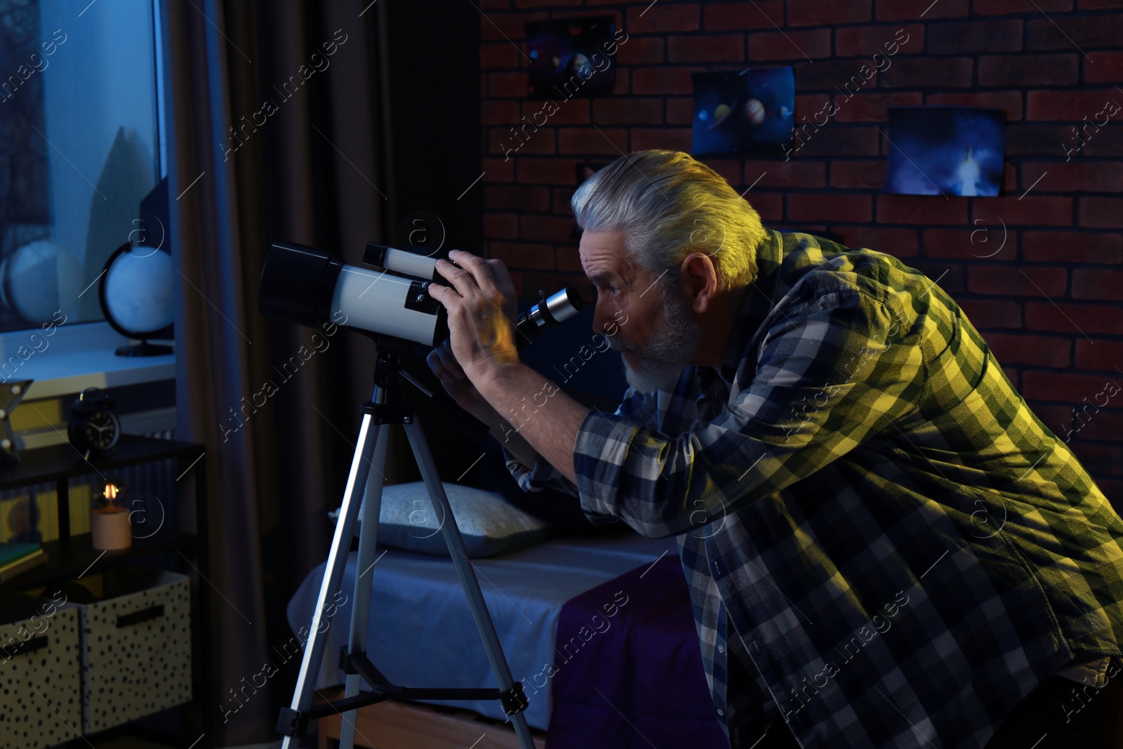 Photo of Senior man looking at stars through telescope in room