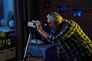 Photo of Senior man looking at stars through telescope in room