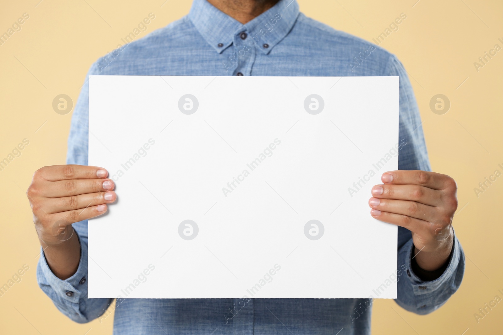 Photo of Man holding sheet of paper on beige background, closeup. Mockup for design