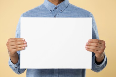 Man holding sheet of paper on beige background, closeup. Mockup for design