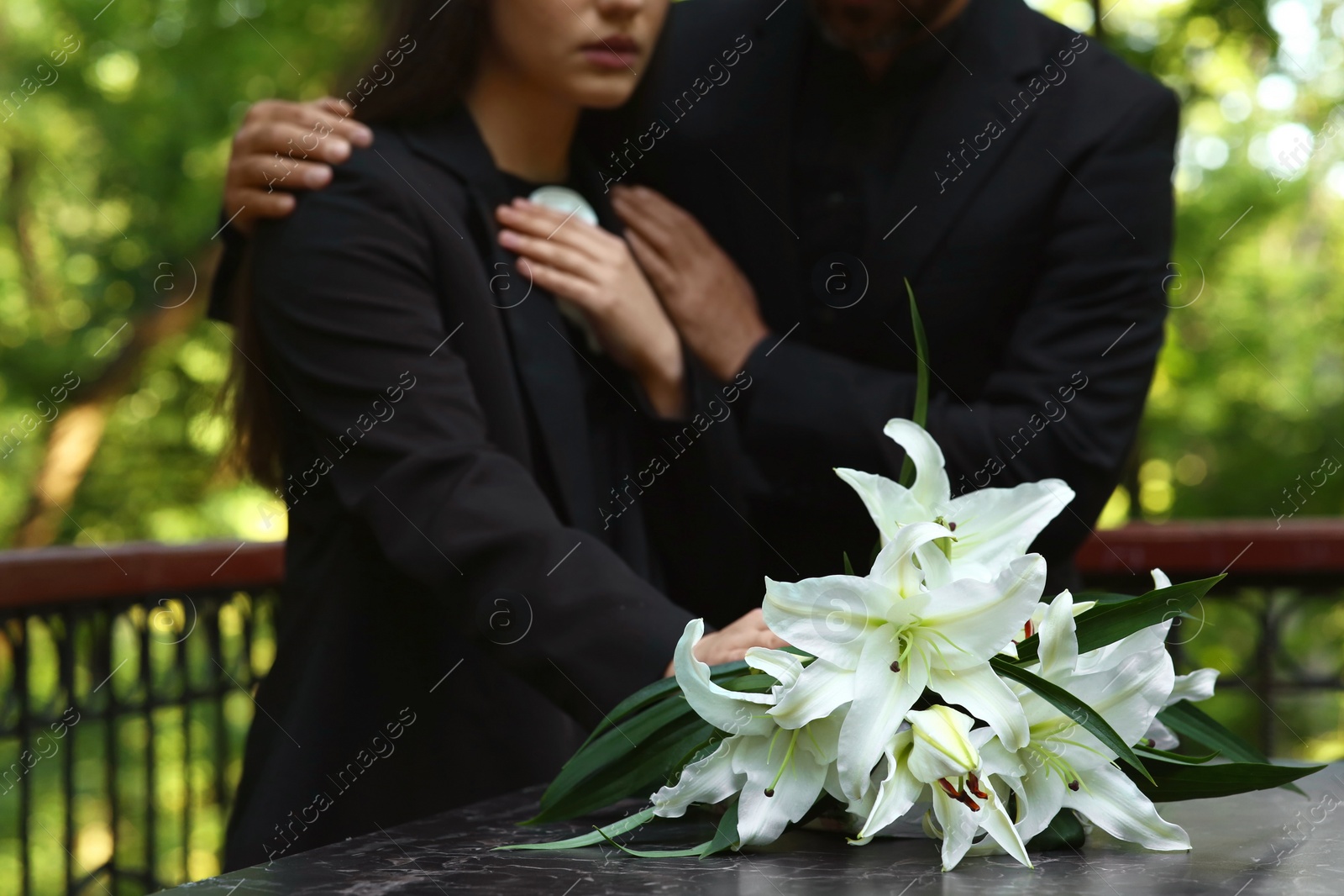 Photo of People near white lilies on tombstone at cemetery, closeup. Funeral ceremony