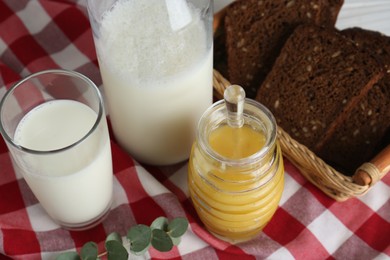 Jar with tasty honey, milk and bread on checkered cloth, above view