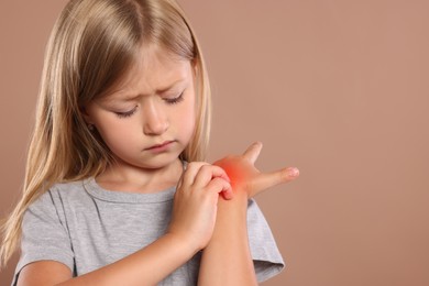 Photo of Suffering from allergy. Little girl scratching her hand on light brown background, space for text
