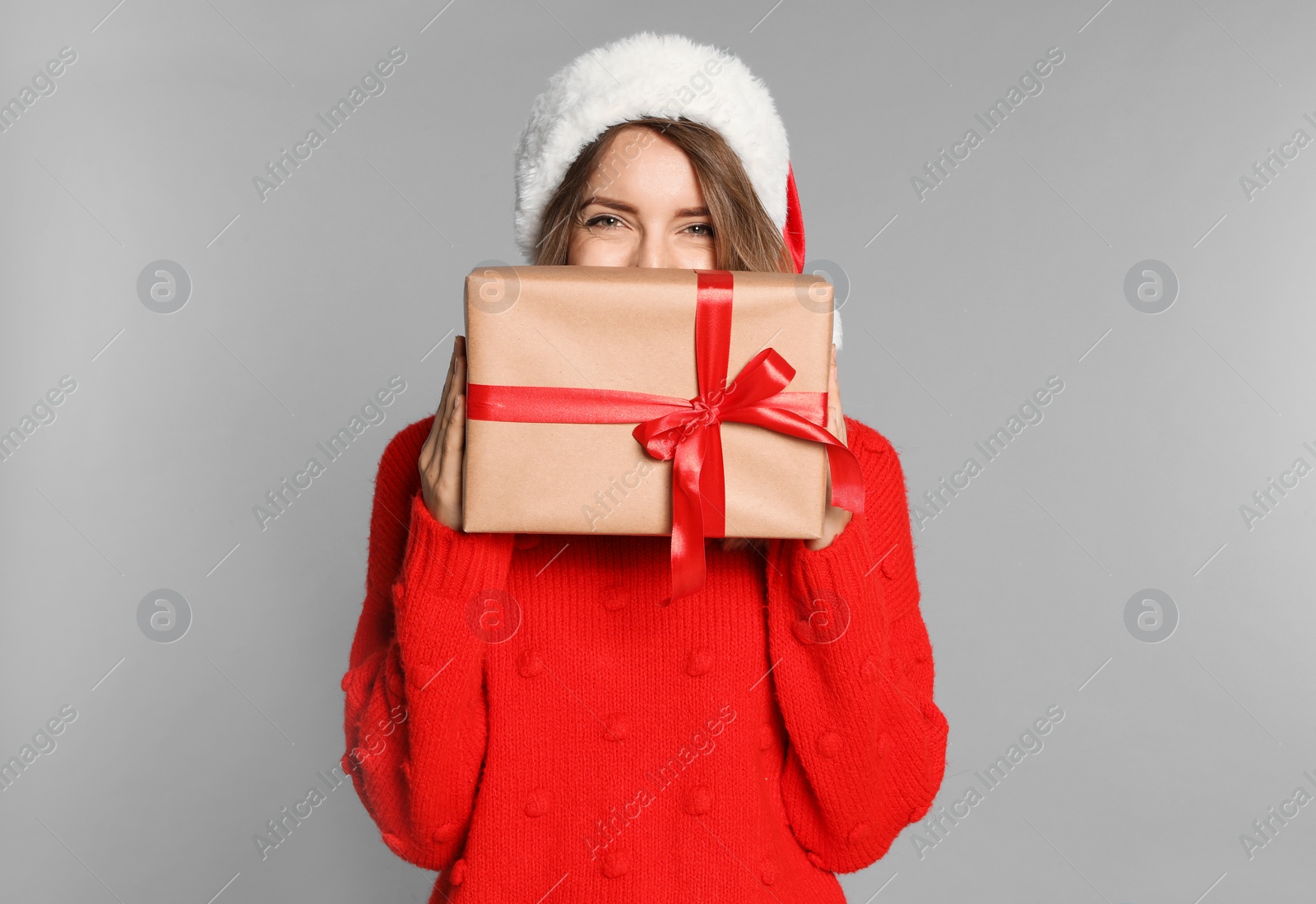 Photo of Happy young woman in Santa hat and sweater with gift box on light grey background. Christmas celebration