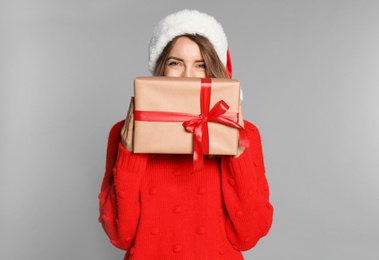 Photo of Happy young woman in Santa hat and sweater with gift box on light grey background. Christmas celebration