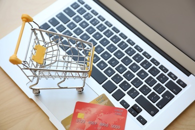 Photo of Internet shopping. Small cart and credit cards on laptop, closeup