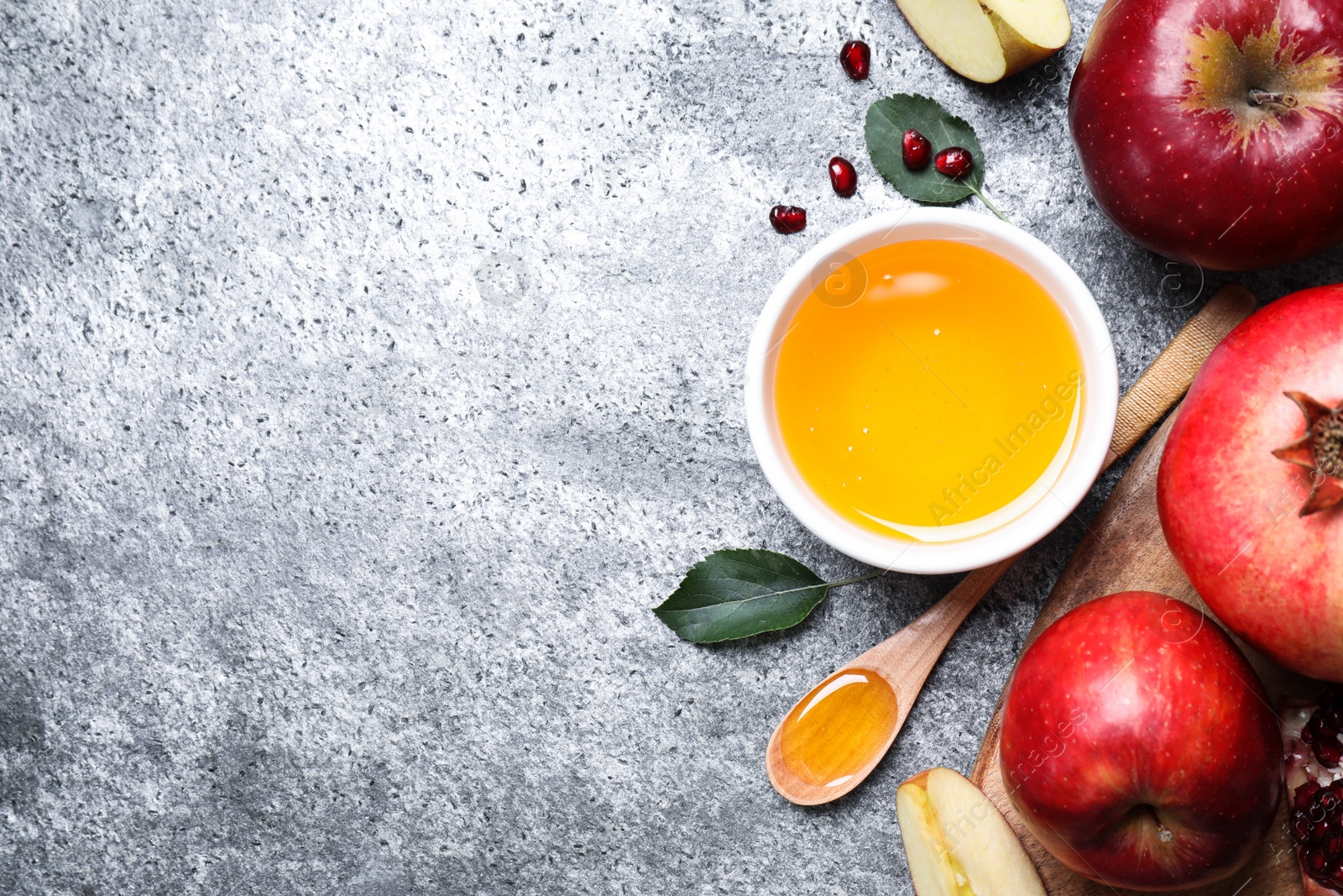 Photo of Honey, apples and pomegranate on grey table, flat lay with space for text. Rosh Hashanah holiday