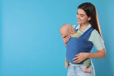 Mother holding her child in sling (baby carrier) on light blue background. Space for text