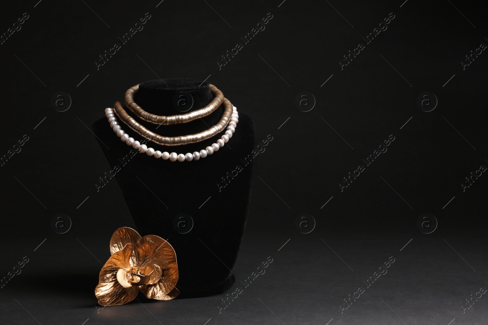 Photo of Stylish necklaces on stand and decorative flower against black background, space for text. Luxury jewelry