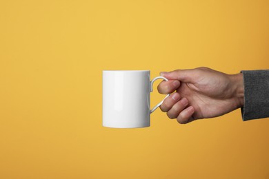 Man holding white mug on yellow background, closeup. Space for text