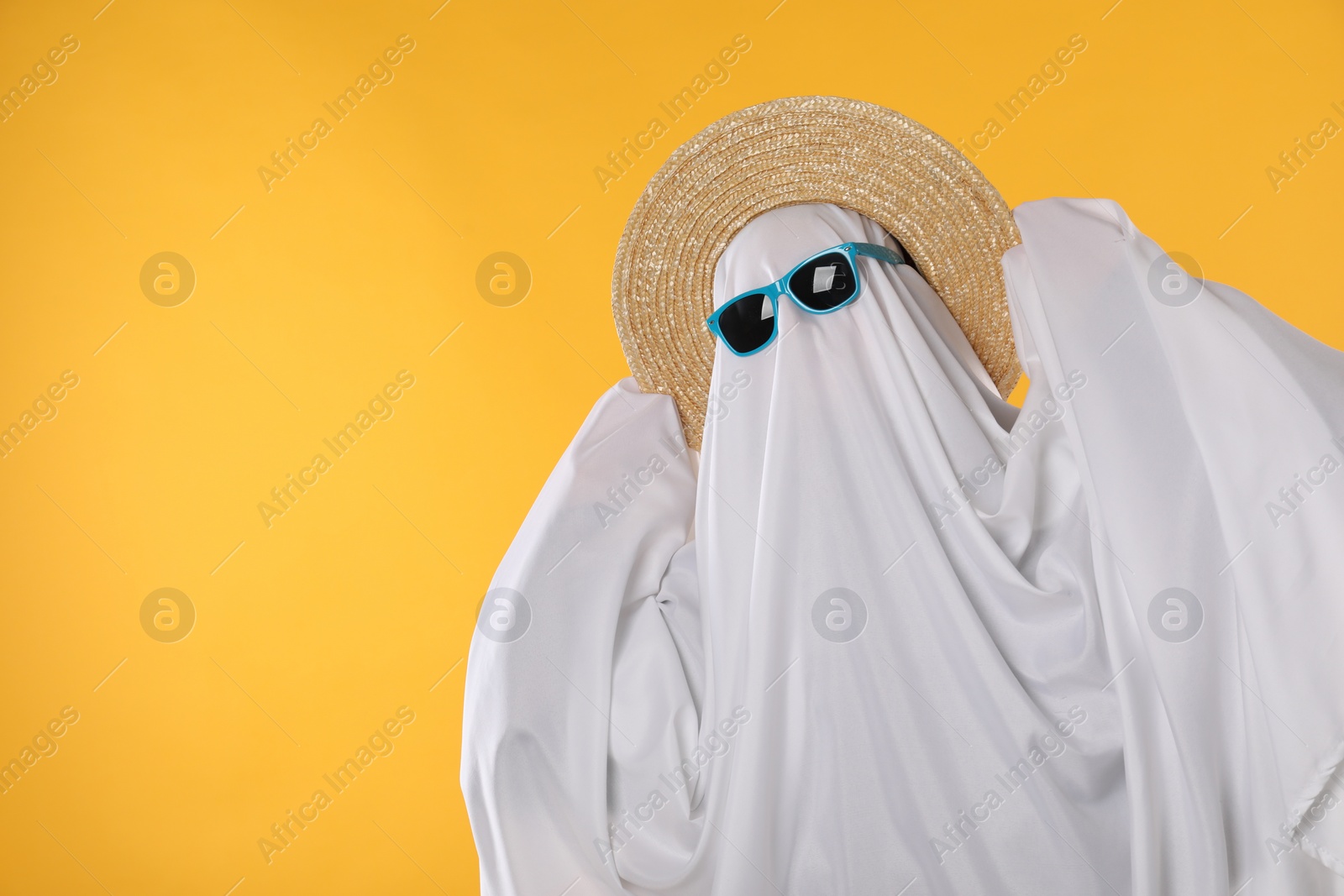 Photo of Person in ghost costume, sunglasses and straw hat on yellow background, space for text