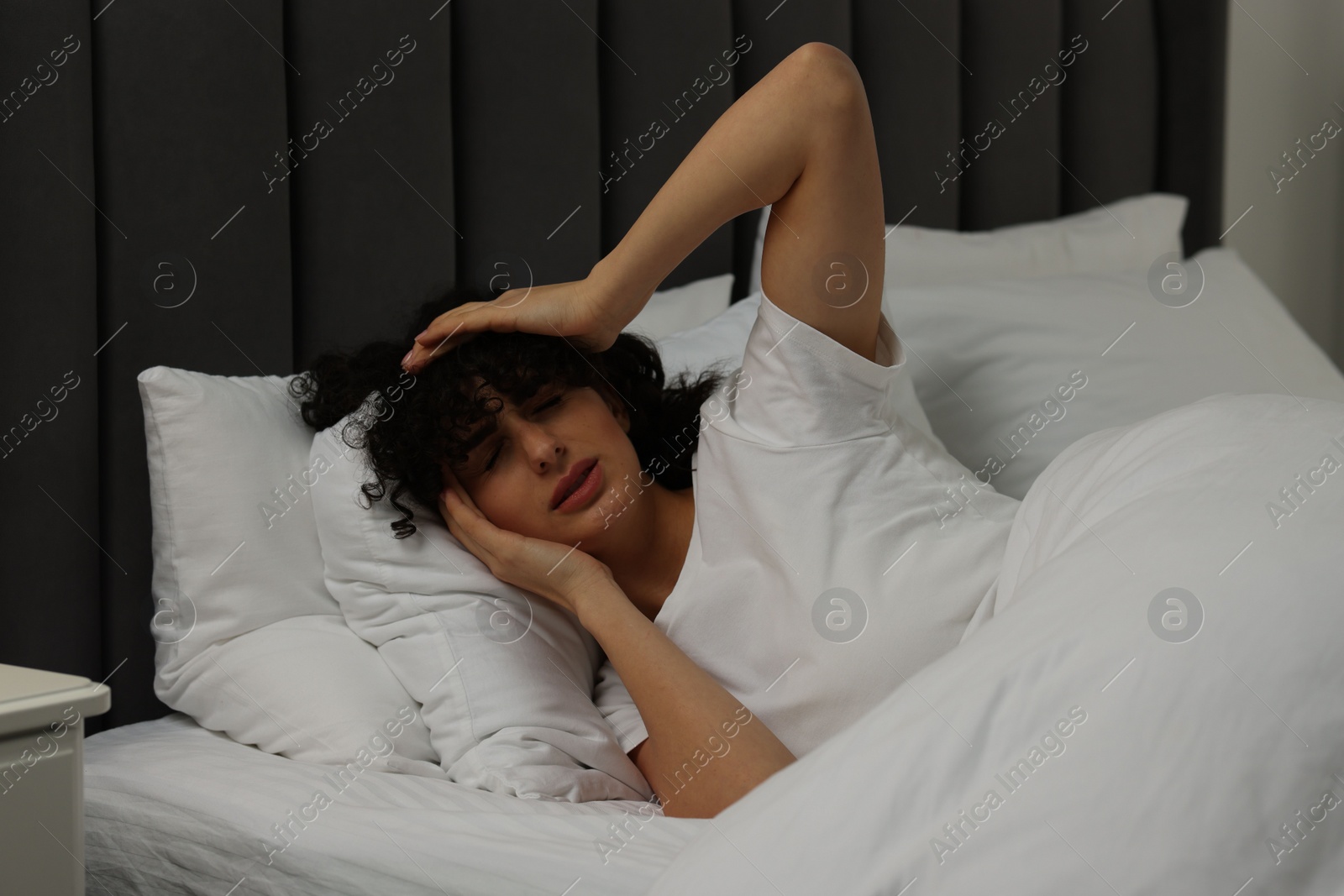 Photo of Young woman suffering from headache in bed at night