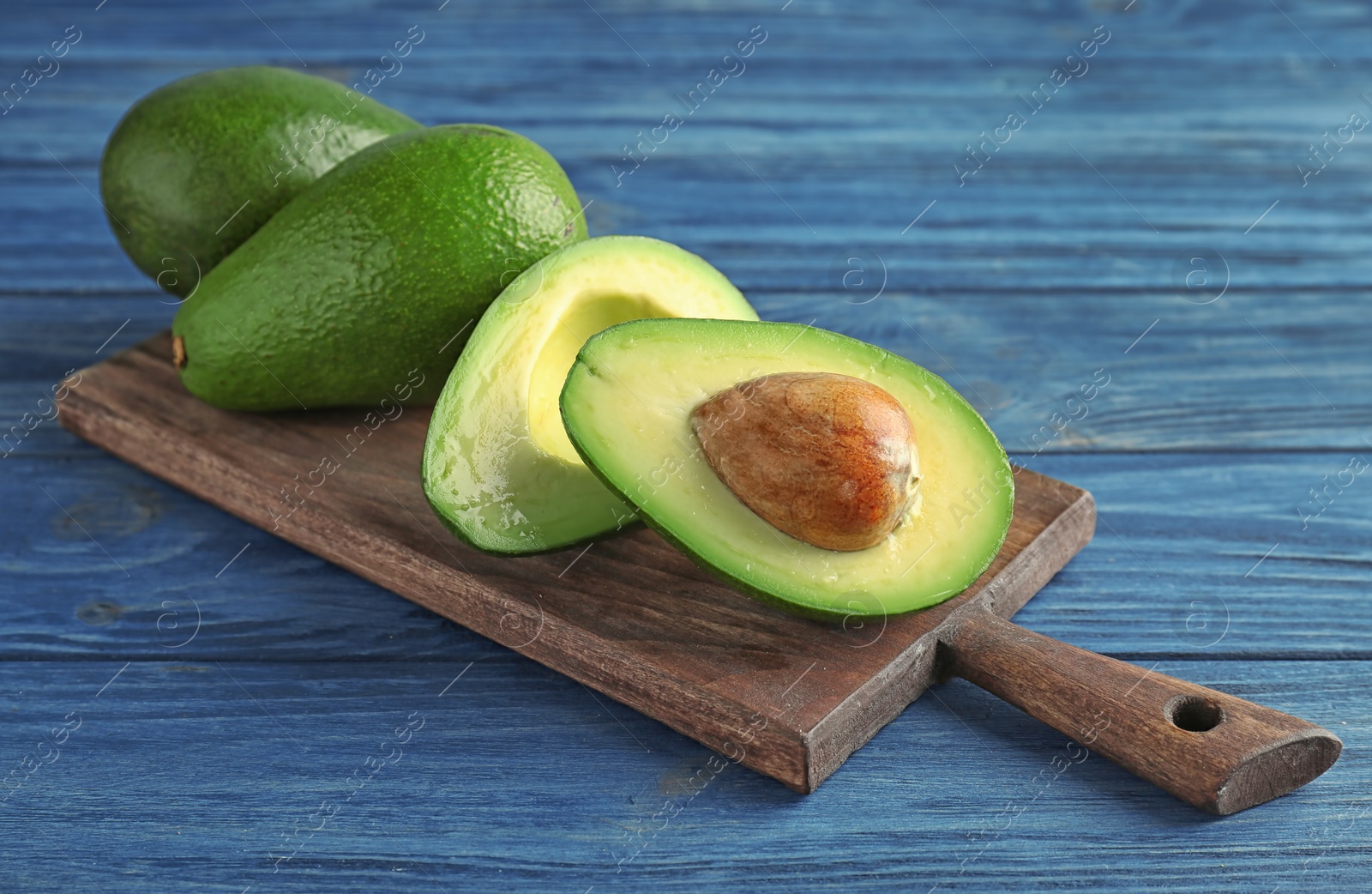 Photo of Board with ripe avocados on wooden background