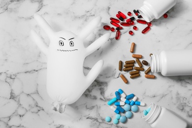Photo of Glove monster and different pills on white marble table, flat lay. Immune system concept