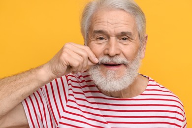 Photo of Senior man touching mustache on orange background