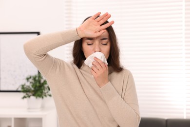 Photo of Sick woman with tissue blowing nose at home. Cold symptoms