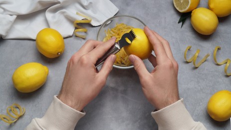 Man zesting lemon at grey table, closeup