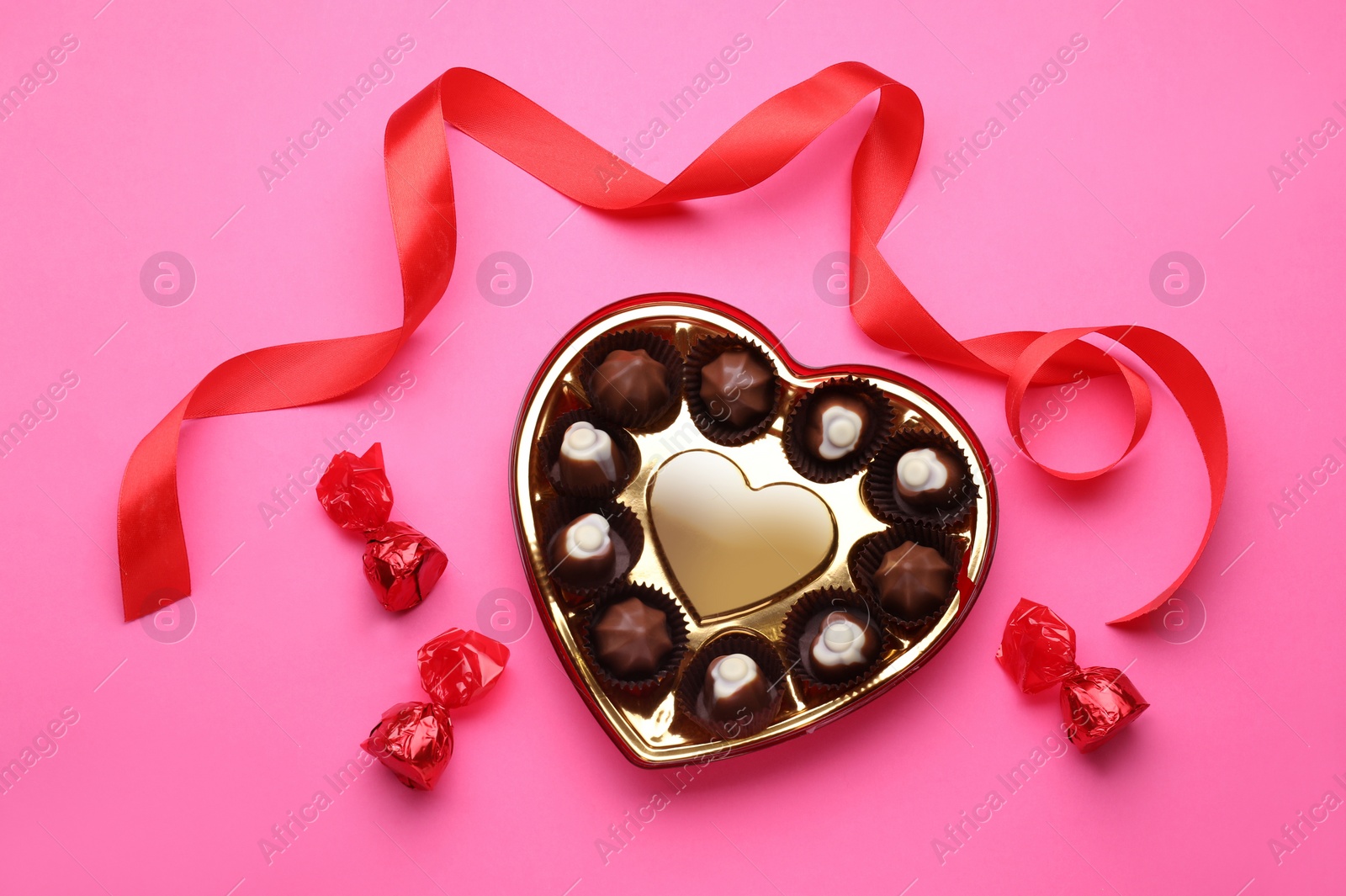 Photo of Heart shaped box with delicious chocolate candies and ribbon on pink background, flat lay