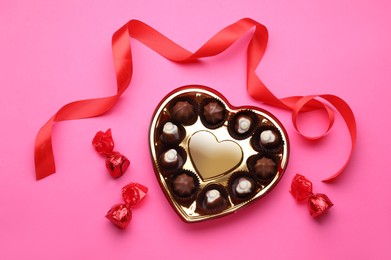 Photo of Heart shaped box with delicious chocolate candies and ribbon on pink background, flat lay