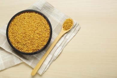 Bowl and spoon with uncooked bulgur on wooden table, flat lay. Space for text