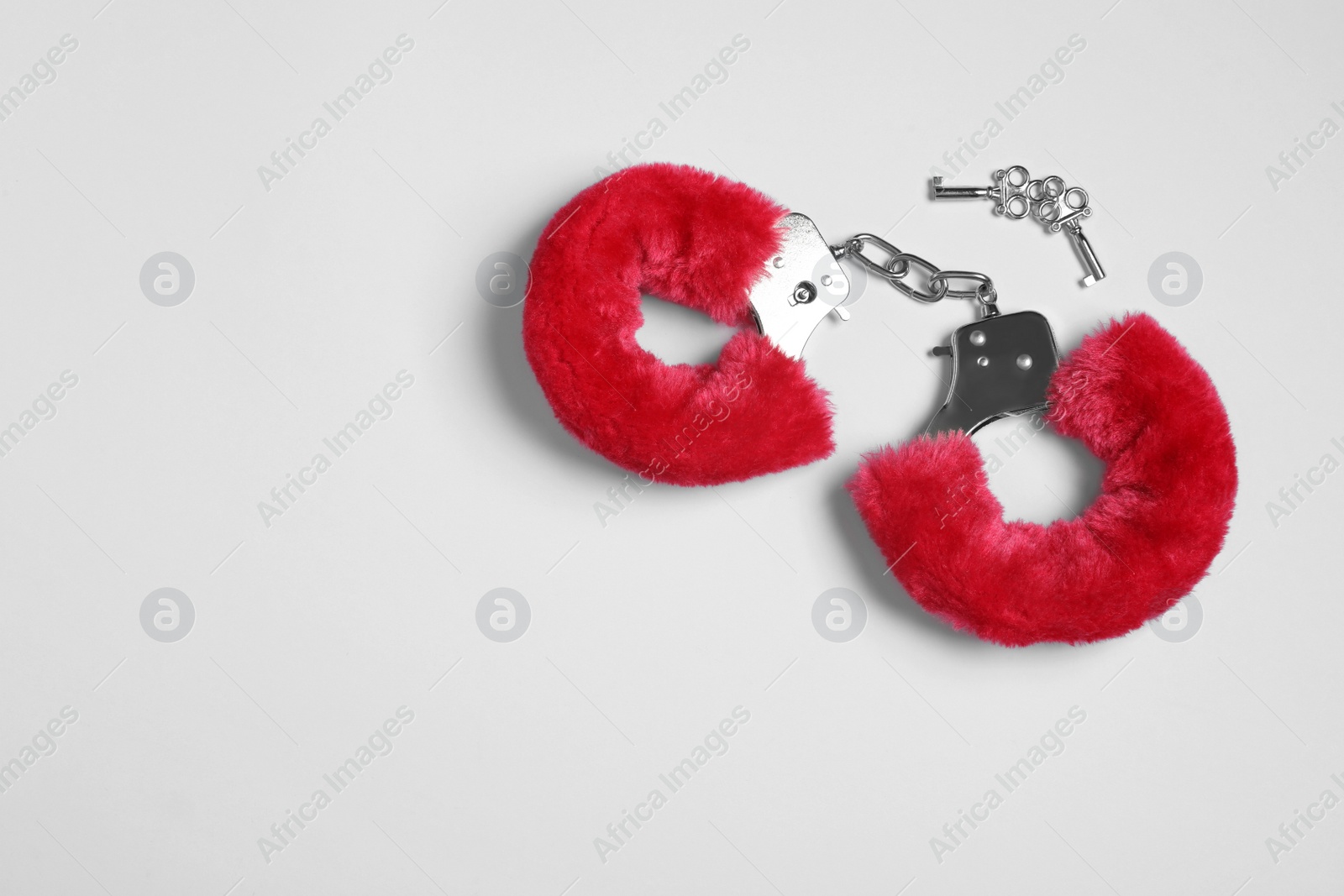 Photo of Red furry handcuffs and keys on white background, top view. Sex toy