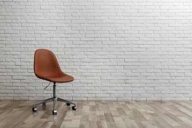Comfortable office chair near white brick wall indoors. Space for text