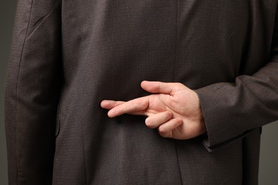 Man crossing fingers behind his back on grey background, closeup