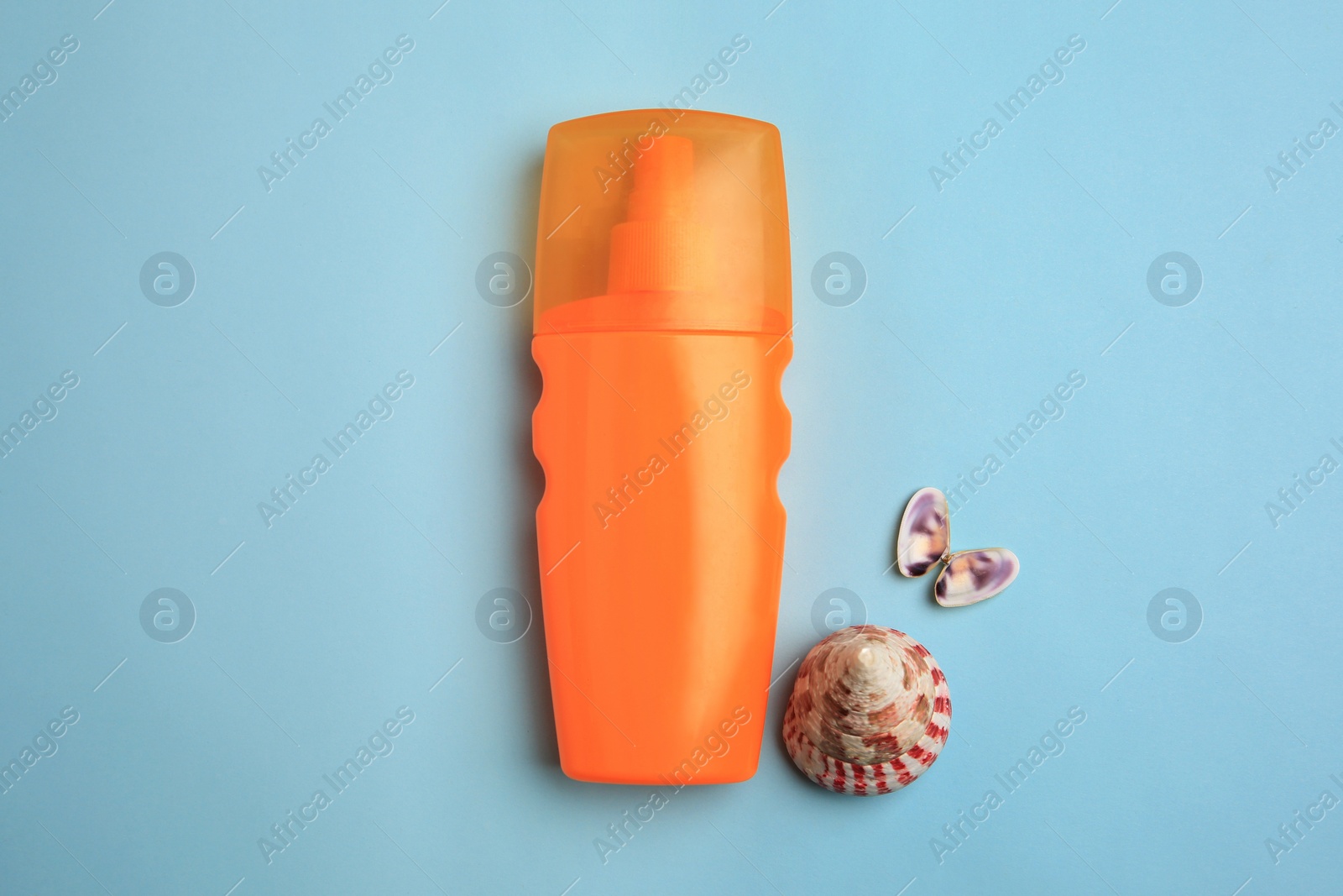 Photo of Bottle of sunscreen and seashells on light blue background, flat lay