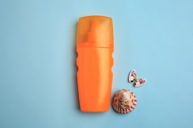 Photo of Bottle of sunscreen and seashells on light blue background, flat lay